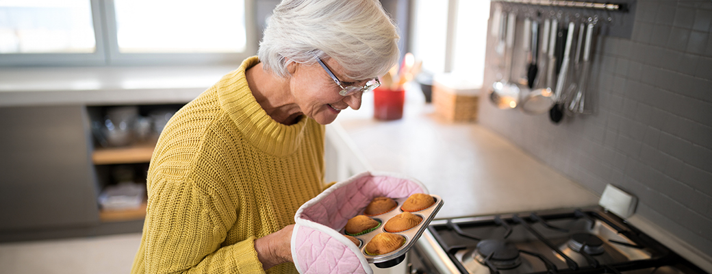 Image of senior woman removing muffins from the oven